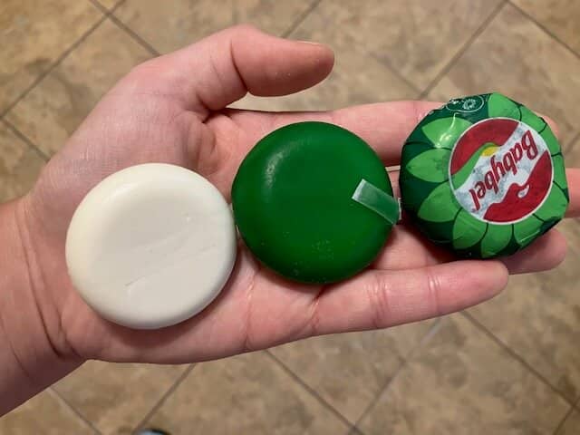 hand holding vegan babybels in 3 ways. 1. full packaging 2. wax case on. 3. just the vegan cheese.