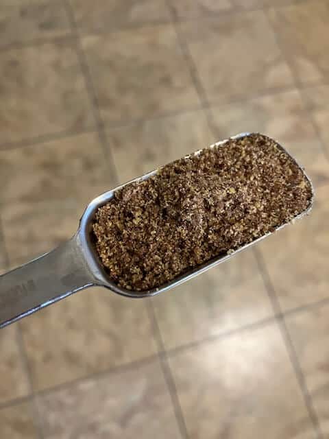 a measuring spoon with ground flaxseeds in it