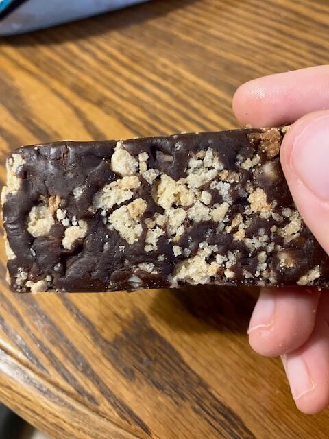 Hand holding lenny and larrys the complete cookie fied bar chocolate almond sea salt flavor
